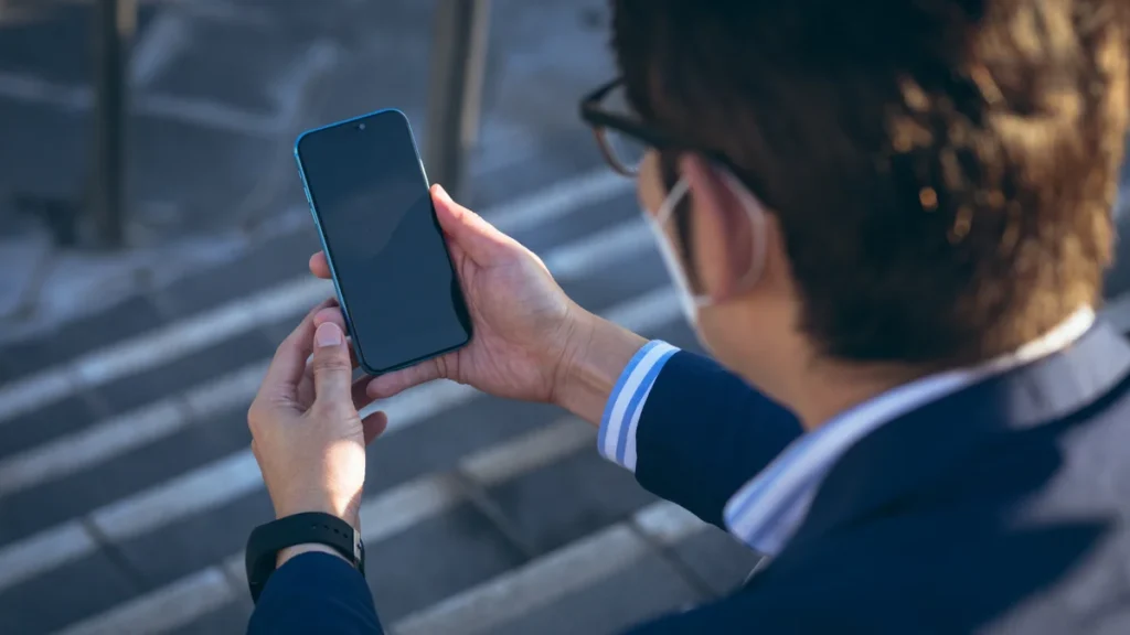 Homme utilisant son smartphone en ville pour rechercher un numéro dans un annuaire inversé gratuit
