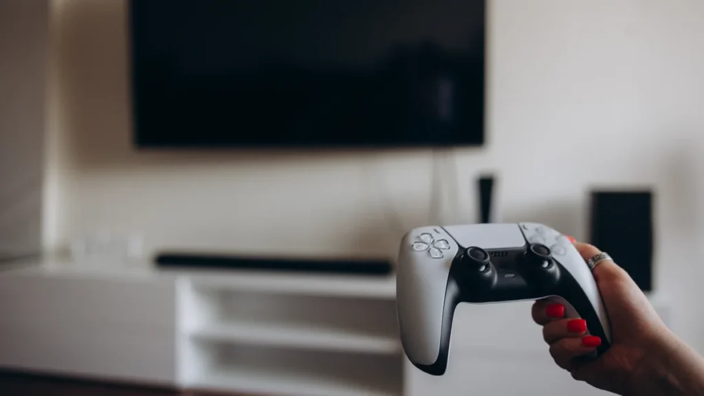 Main tenant une manette de console blanche devant un téléviseur, avant de connecter sa PS5 à internet
