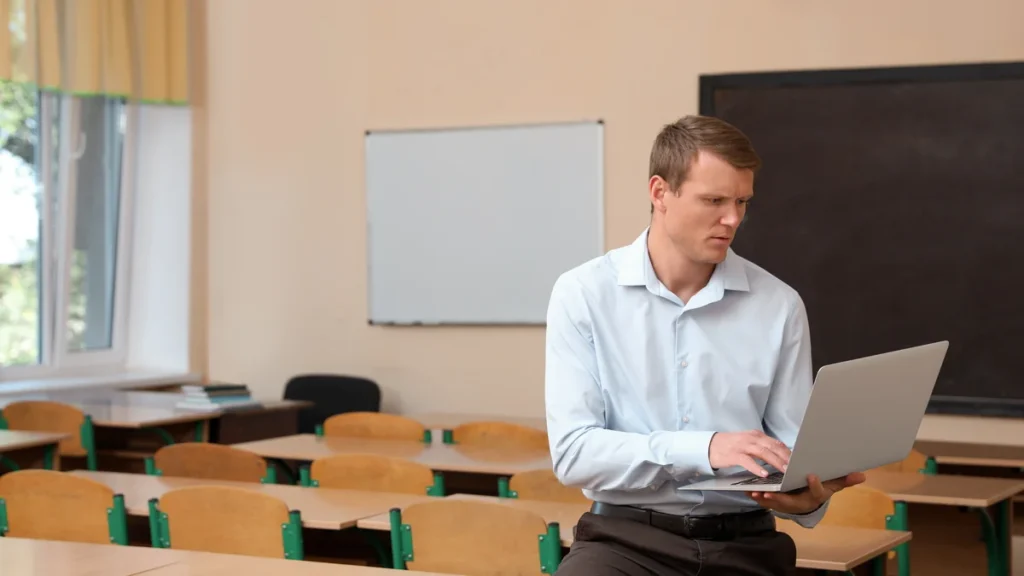 Enseignant consultant le webmail académique sur un ordinateur portable dans une salle de classe vide