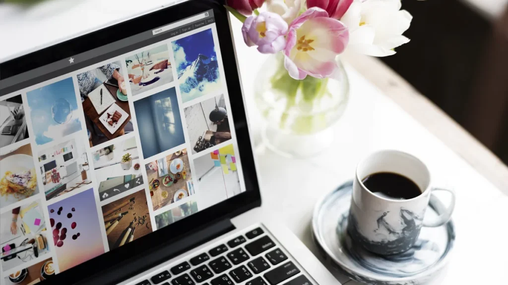 Ordinateur portable affichant une galerie de photos en ligne, à côté d’un bouquet de tulipes et d’une tasse de café